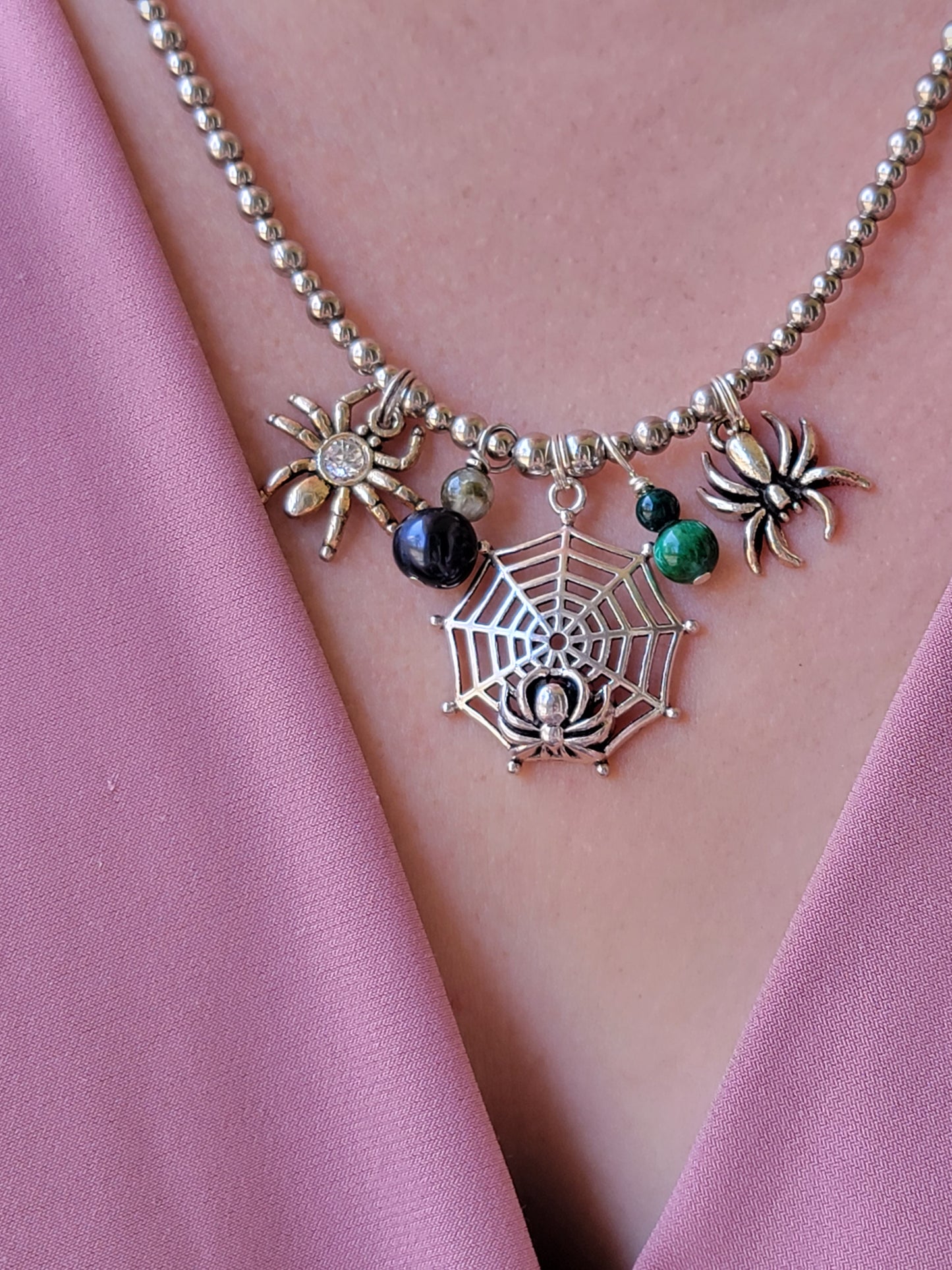 Silver necklace with spider and web charms on a pink fabric background