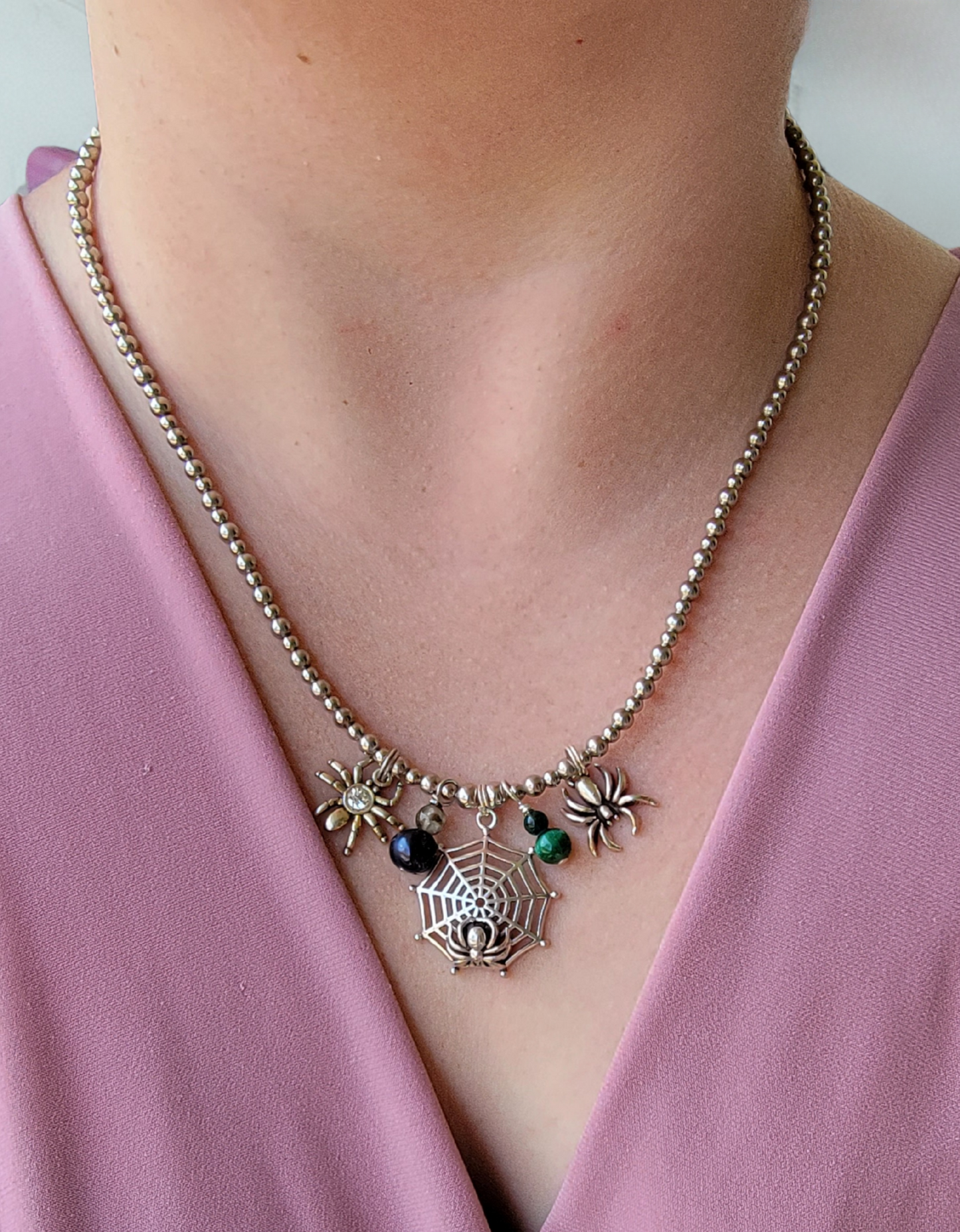 Necklace with spider web and spider charms worn by a person in a pink top.