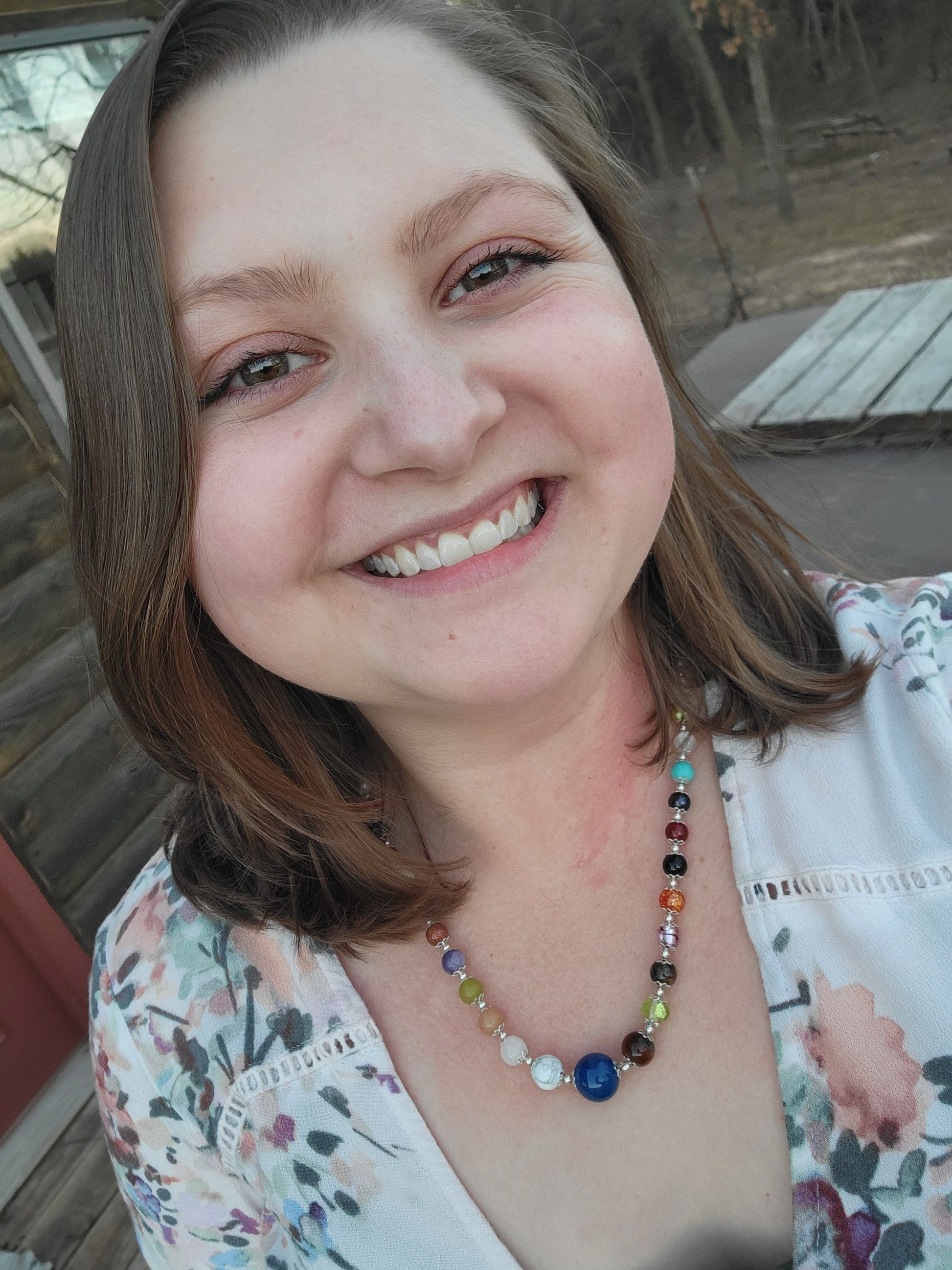 Woman wearing a colorful beaded necklace with a floral-patterned top.